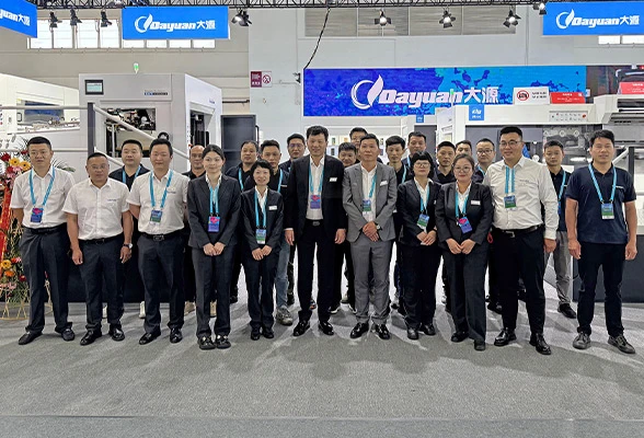 Dayuan team photo at an industrial exhibition booth with die-cutting machines