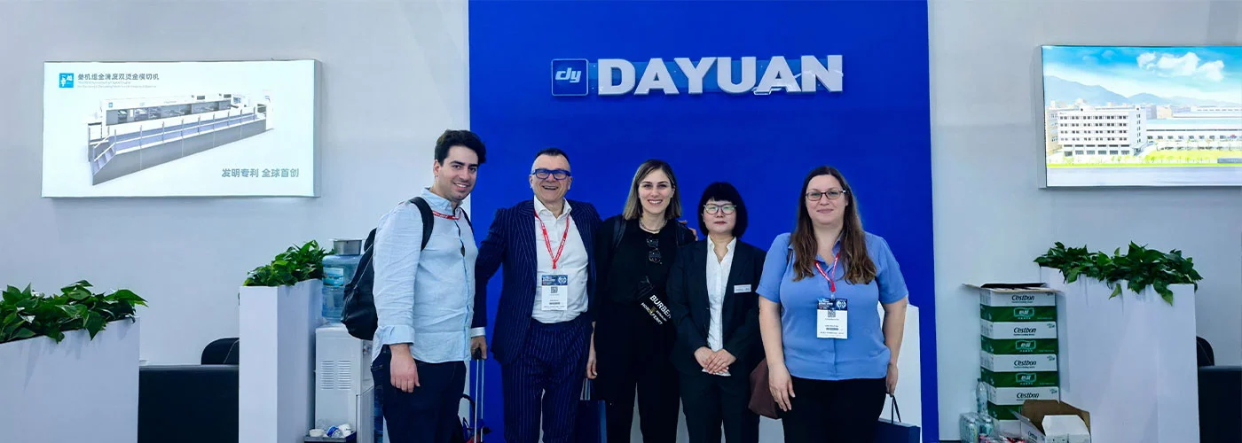 Dayuan team photo with international clients in front of the DAYUAN logo wall at exhibition booth