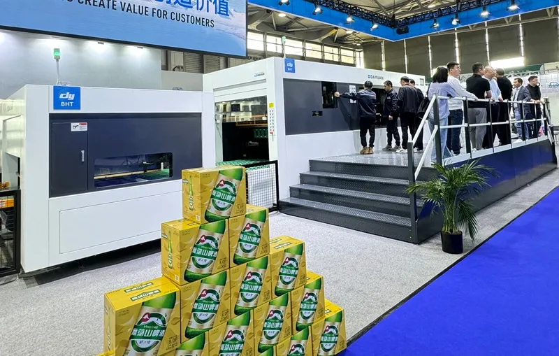 Dayuan BHT corrugated die-cutting line displayed at packaging expo, finished beer cases as application showcase, professional visitors on observation platform